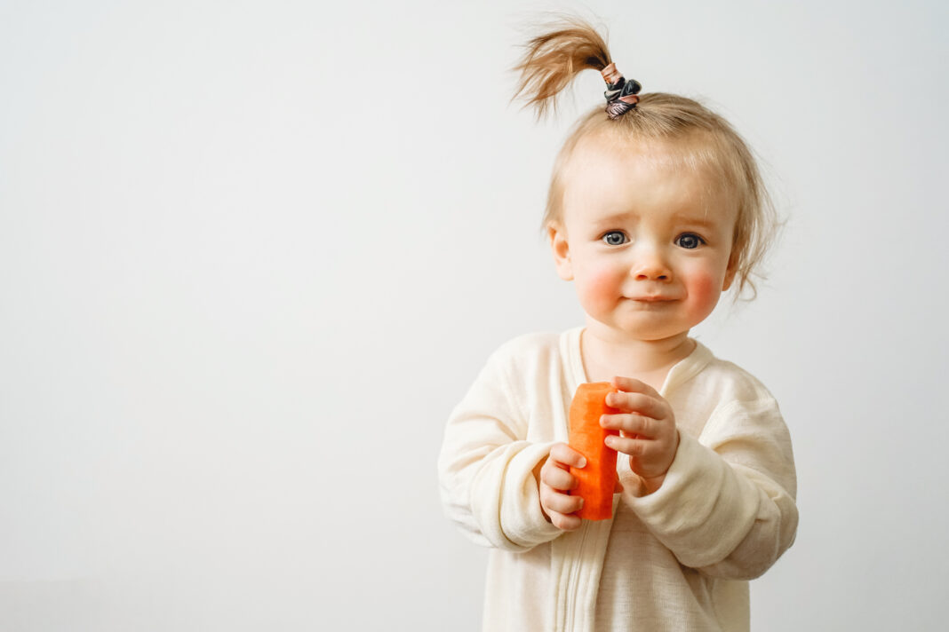 a baby with a food allergy holds a carrot in her hands, the chil