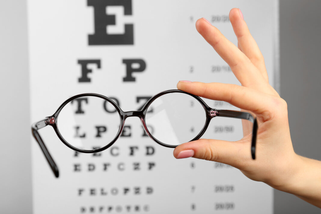 Glasses in hands on eye chart background, close-up